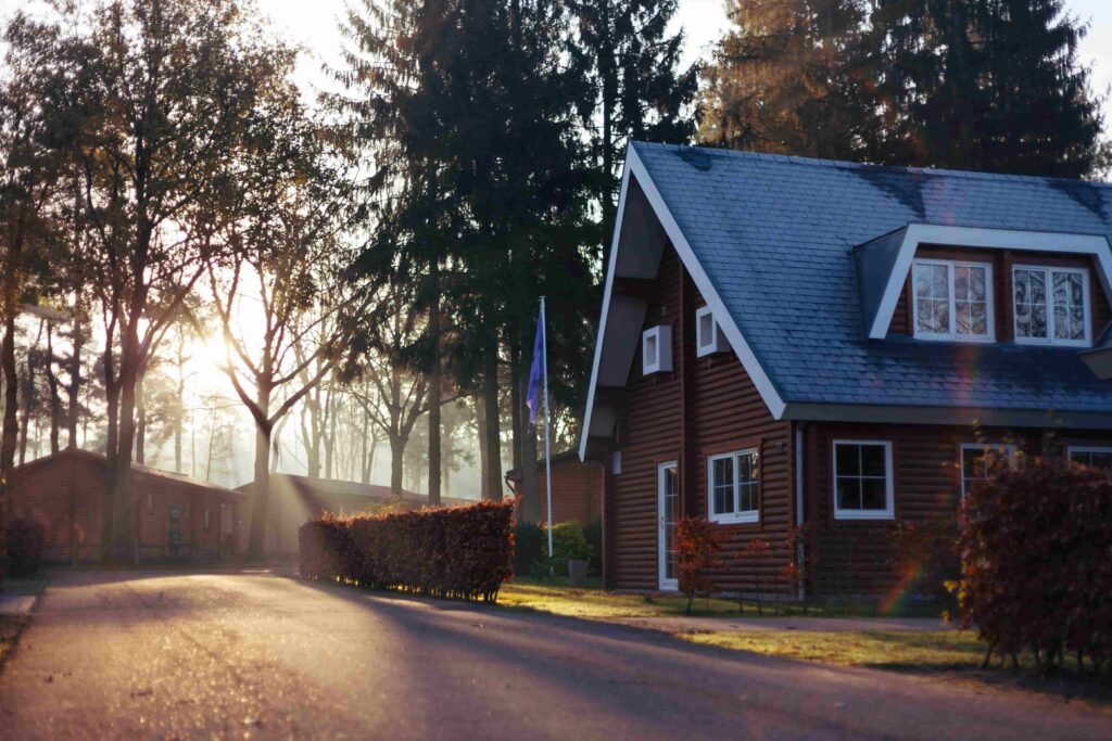 Shelter and Movement. A timber house with a steep grey roof on a quiet, tree-lined street