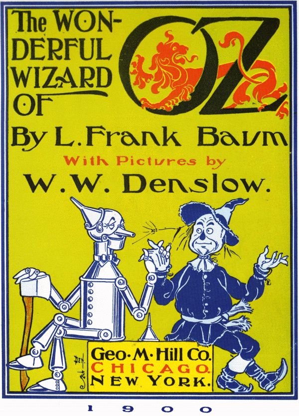 The Wonderful Wizard of Oz 1900 first-edition cover by W. W. Denslow: on a yellow-green background, hand-lettered black type reads "The Wonderful Wizard of Oz, by L. Frank Baum, with pictures by W. W. Denslow", with a red lion inside the large letters "OZ". Below, the Tin Woodman, holding an oil can and resting on his axe, shakes hands with the Scarecrow. A label at the bottom reads "Geo. M. Hill Co., Chicago, New York", above the year 1900.